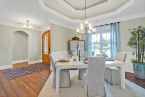Bright elegant dining room with white table, gray chairs, tray ceiling, and coastal blue accents