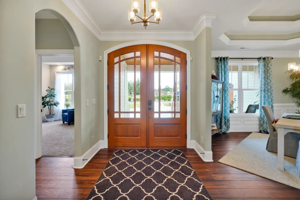 Bright entryway with wooden double doors, glass panels, hardwood floors, and elegant chandelier.