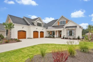 Modern suburban stone-front home with three-car garage and manicured lawn under a clear blue sky.