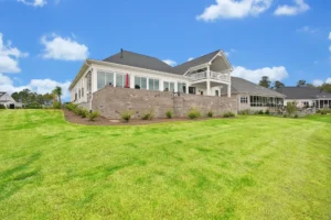 Modern suburban home with stone retaining wall, lush green lawn, and spacious sunny patio.