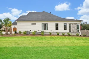 Single-story white house with gray roof, green lawn, and palm tree under blue sky.