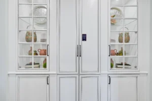 Modern white built-in cabinet with glass shelves displaying ceramics, plants, and books.