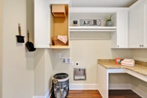Modern white laundry room with granite countertops, pink towels, and organized open shelving.