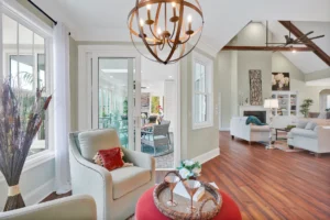 Bright modern living room with vaulted ceilings, natural light, cream chairs, red ottoman, and wood floors.