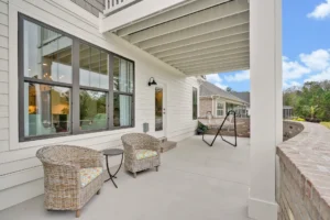 Modern coastal patio with wicker chairs, hanging swing, and concrete floor beside white home.