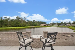 Peaceful lakeside patio with cushioned chairs, small table, and scenic pond view.
