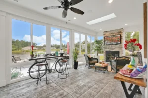 Bright sunroom with stone fireplace, large windows, rustic flooring, and cozy seating filled with sunlight.