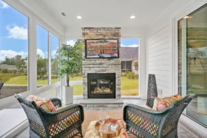 Bright sunroom with stone fireplace, wicker chairs, and large windows filled with natural light.