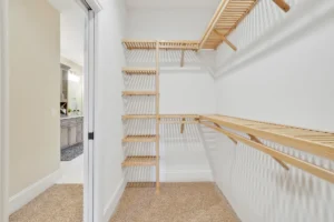 Spacious modern walk-in closet with light wood shelving, white walls, and beige carpet.