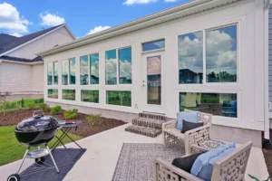 Modern backyard patio with cushioned chairs, grill, and large reflective windows for outdoor relaxation.
