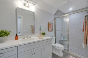 Modern gray bathroom with glass shower, white vanity, warm lighting, and minimalist decor.