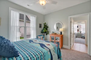 Bright coastal bedroom with soft blue walls, ocean-inspired quilt, and natural light-filled decor.
