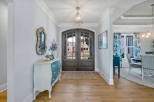 Bright coastal entryway with wooden doors, teal console, and open dining area filled with light.