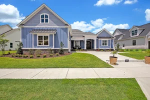 Blue modern farmhouse exterior with white trim, landscaped lawn, and bright sky in Wilmington NC.