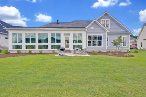 Modern suburban home with sunroom, patio, and lush green backyard under a bright sky.