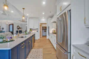 Bright modern kitchen with navy island, gold accents, white cabinets, and stainless steel appliances.