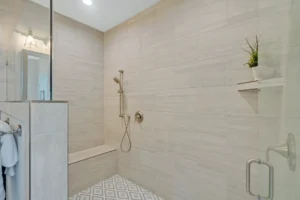 Modern beige tile walk-in shower with glass door, built-in bench, and brushed metal fixtures.