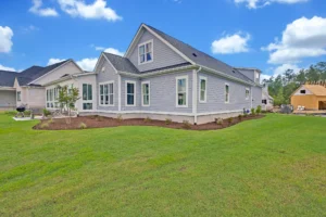 Modern gray suburban house with white trim, dark roof, and large green front lawn.