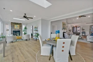 Bright open-concept living and dining room with light wood floors and stone fireplace.