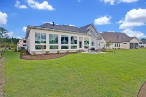 Modern single-story suburban home with large windows, lush green lawn, and outdoor seating area.