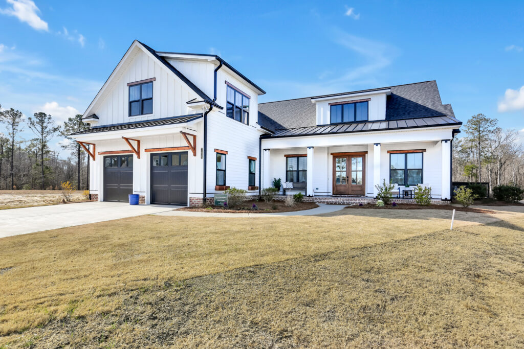 Modern white farmhouse with black trim, wood accents, and covered porch under clear blue sky.