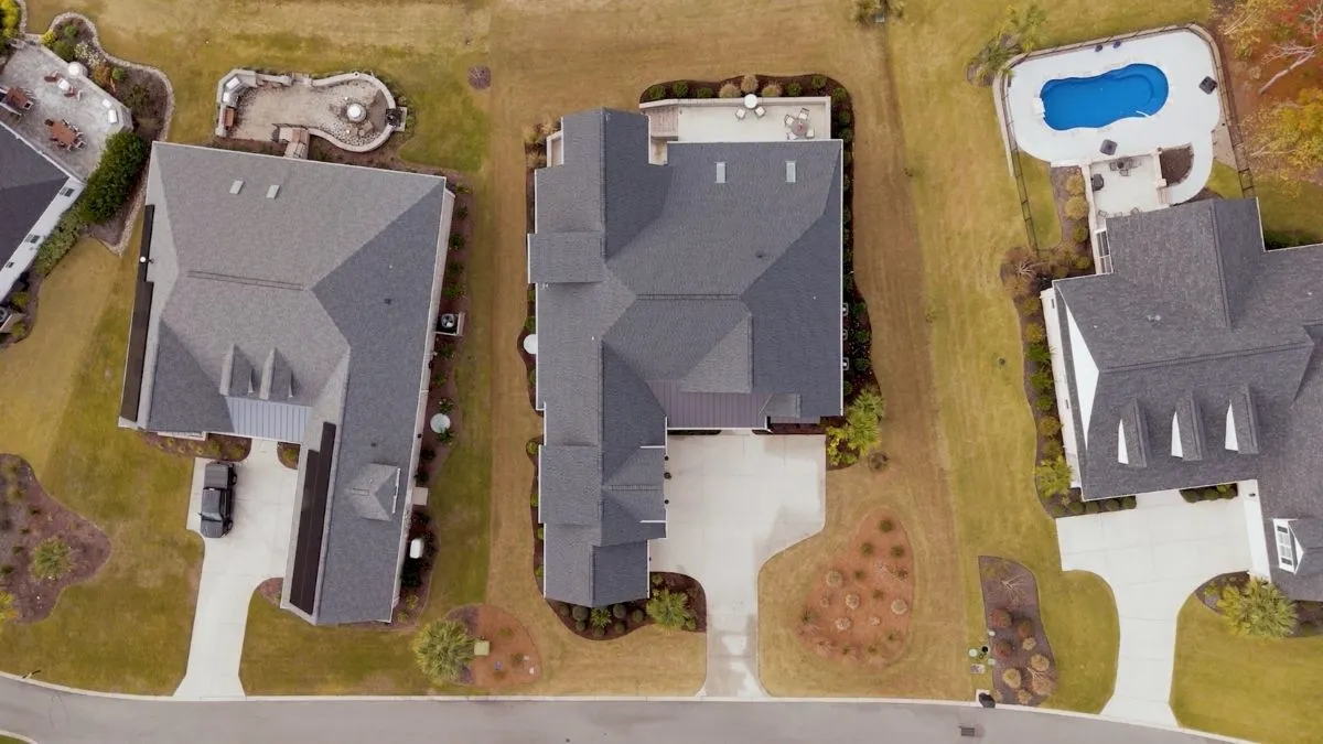 5 Mistakes to Avoid When Buying a Lot Before Choosing a Custom Home Builder 1 : Aerial top-down view of suburban luxury homes with custom roofs, driveways, landscaped yards, and a swimming pool.