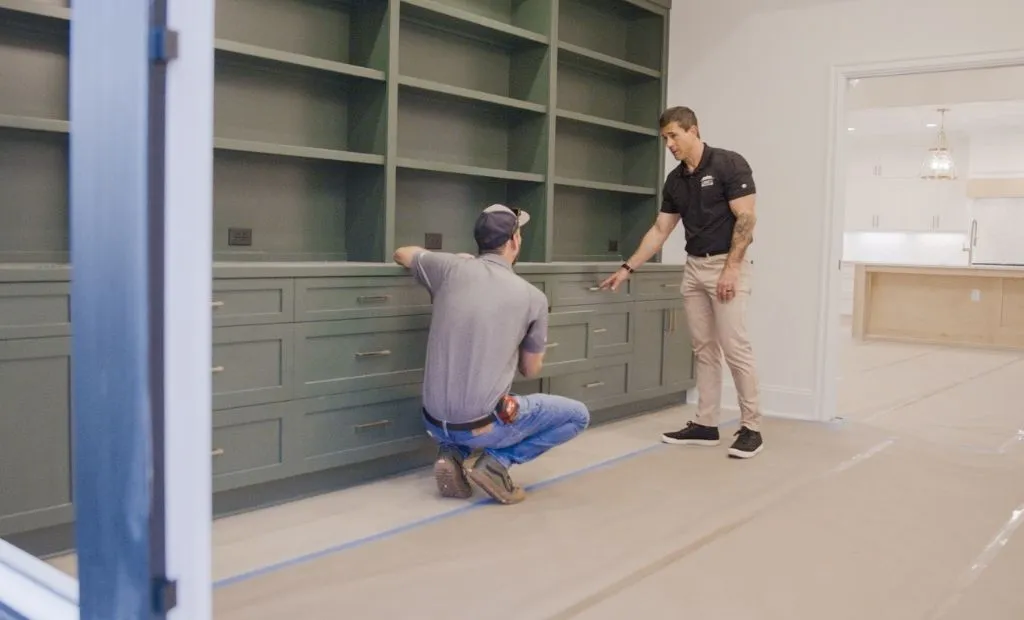 Best Questions to Ask Before Choosing a Luxury Home Builder 1 Two workers inspect custom olive green cabinetry and shelving built into a wall.