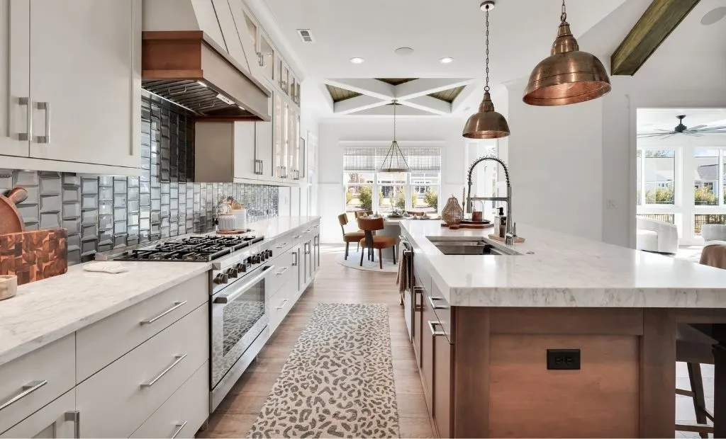 Modern kitchen with white cabinets, marble countertops, copper pendant lights, and a wooden island.