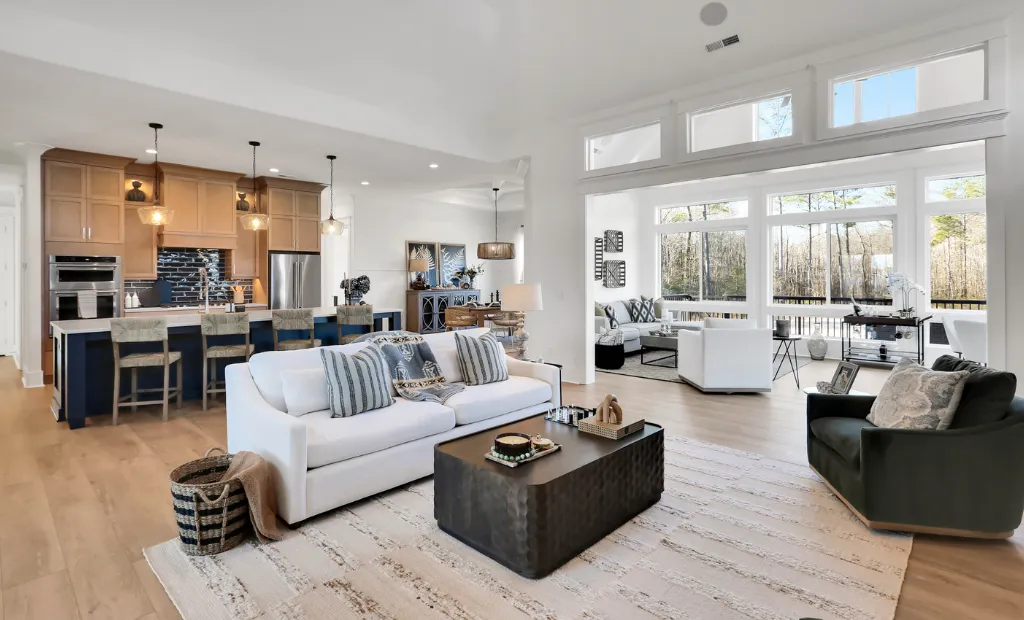 Spacious, open-concept living room and kitchen with white sofas, warm wood cabinets, and large windows.