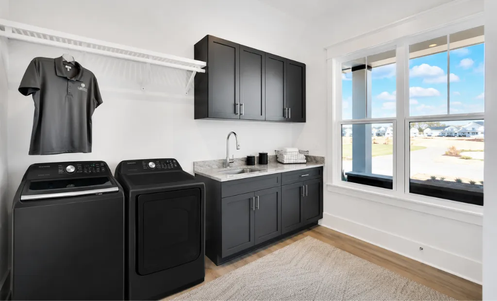 Best Floor Plan Features for a Forever Home 1 Modern laundry room featuring matte black appliances, dark gray cabinets, a sink, and a bright window.